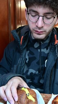 Caucasian man with glasses eating a delicious italian croissant filled with custard at the bar. Morning routine in a typical cafe, a moment of pleasure enjoying a sweet pastry with pleasure