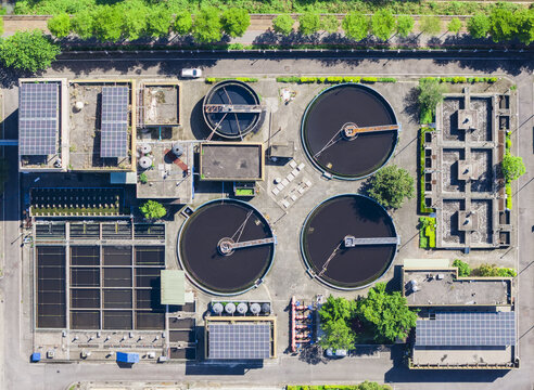 Aerial view of a wastewater treatment plant featuring circular clarifier tanks, rectangular filtration beds, and solar panels on rooftops surrounded by lush green trees Taiwan.
