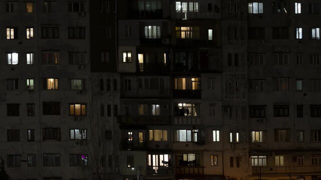Timelapse of lights in windows turning on and off in residential building house in evening or at night