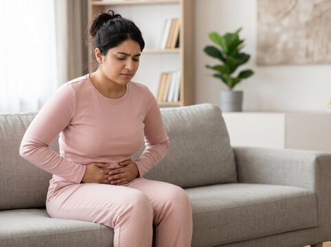 woman sitting on sofa holding stomach in pain representing menstrual cramps ovulation discomfort and women healthcare concept