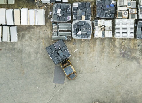 Aerial view of a yellow forklift moving stacks of old televisions and monitors on pallets at a home appliance recycling plant in Taiwan.