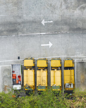Aerial view of yellow garbage trucks and a recycling truck parked on a concrete lot with white directional arrows in Taiwan.