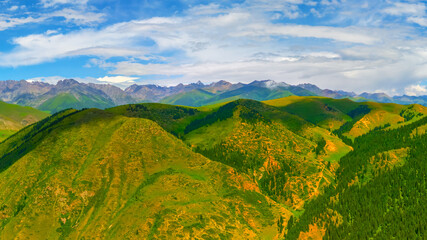 Obraz premium Expansive green hills with distant mountains under cloudy sky