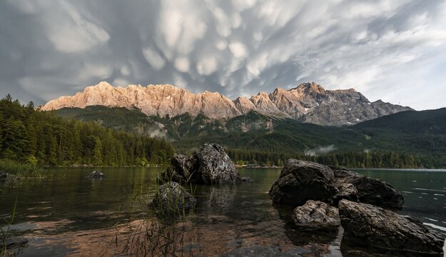 Rocks on the shore, Eibsee lake in front of Zugspitze massif with Zugspitze, sunset, dramatic Mammaten clouds, Wetterstein range, near Grainau, Upper Bavaria, Bavaria