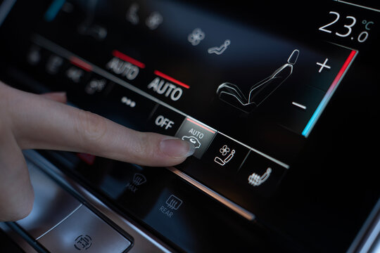 Close-up of finger pressing automatic air recirculation button on climate control touchscreen in modern car, with seat and temperature settings visible.