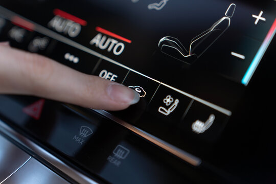 Close-up of finger pressing automatic air recirculation button on climate control touchscreen in modern car, with seat and temperature settings visible.