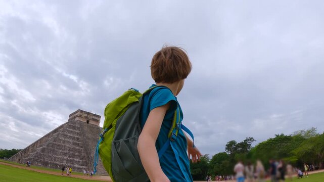 A boy recording himself on action camera while walking in front of Kukulkan pyramid in Chichen Itza, Mexico. Travel vlog, childhood adventure and tourism content creator concept. Slowmotion video.