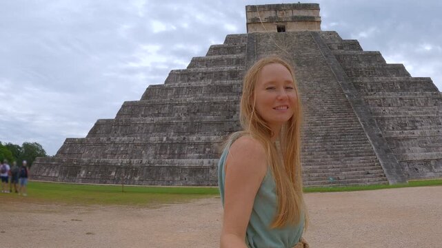 Woman traveler is walking in front of Kukulkan pyramid in Chichen Itza, Mexico. Female tourist recording a selfie video. Slowmotion shot.