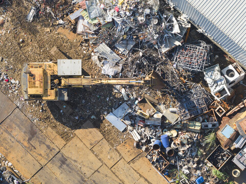 Aerial view of a resource recovery plant with a yellow excavator sorting through piles of scrap metal and industrial debris Taiwan.