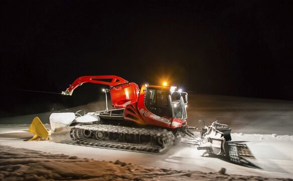 Snowcat planing ski slope with rope at night, Austria