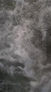 Slow motion of a detailed close-up of bubbling water and foam, capturing the dynamic and abstract patterns formed by the movement.