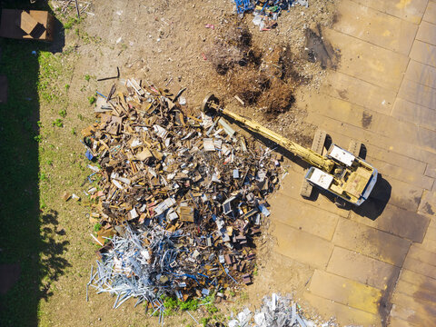 Aerial view of a resource recovery plant with a yellow excavator sorting through a large pile of scrap metal in Taiwan.