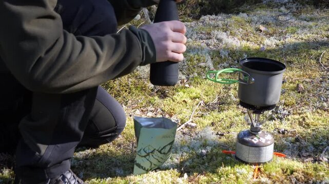 Pouring water from thermos into pot on camping gas stove