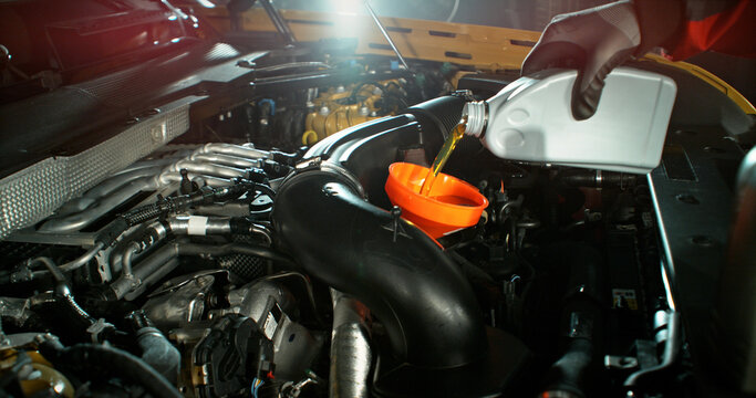 Mechanic pouring engine oil into car engine in workshop. Automotive maintenance, oil change service and professional repair concept with dramatic lighting.