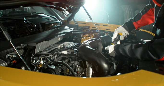 Mechanic repairing car engine in workshop, using tools with dramatic lighting. Automotive maintenance and professional service concept.