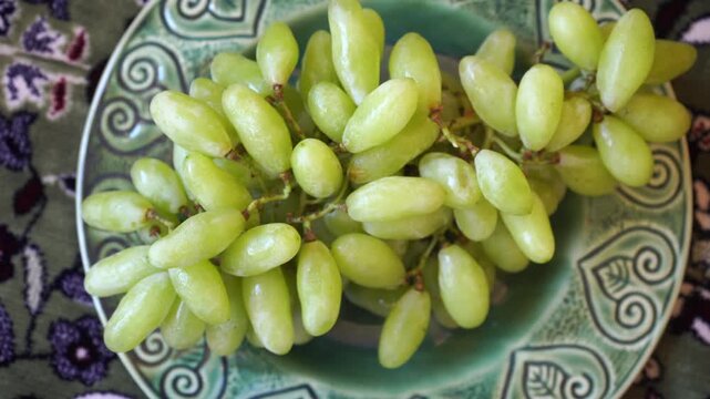 Fresh bunch of grapes on a green ceramic plate over a floral patterned rug background