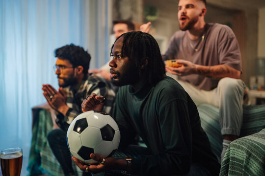 Diverse men watching live soccer game at home, feeling excitement and anticipation during sport event