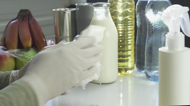 Disinfecting groceries with spray sanitizer during pandemic. Various food containers, including water bottles and oil, sit on a white table awaiting sanitization to ensure safety and hygiene.