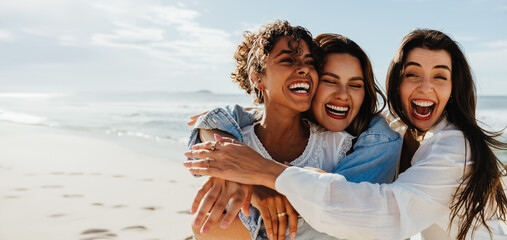 Three friends laughing and hugging together on a bright sunny beach