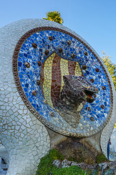 Park Guell,Barcelona,Spain,Mosaic sculpture featuring a dragon head and shield with Catalan flag colors in an outdoor park setting