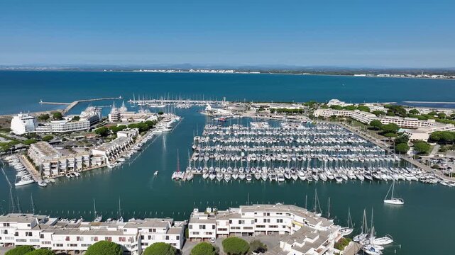 Aerial view of Grau du Roi France with expansive Port Camargue marina rows of sailboats and yachts white residential buildings along canals and vast open sea under clear blue sky