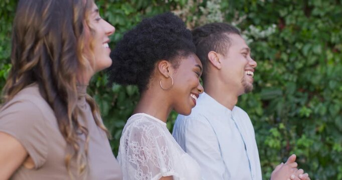 Vertical video: Diverse friends clapping and laughing, applauding off-camera speaker by hedge