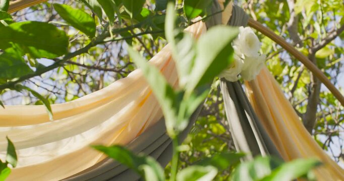 Draped fabrics swaying with breeze and camera pan, revealing white roses at knot for garden decor