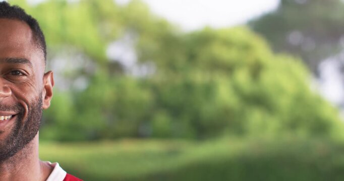 Mature African-American man smiling, being filmed at park in red jersey with white trim, copy space
