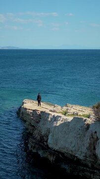 Lone figure stands on rocky outcrop overlooking vast blue ocean expanse