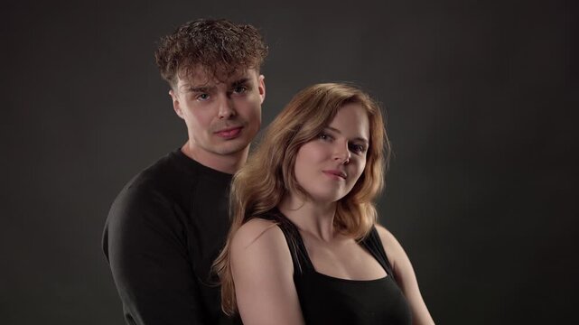 Beautiful young man and woman hugging tenderly while posing together against a gray background