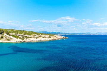 Fototapeta premium Expansive blue ocean meets a rugged, green coastline with distant wind turbines on the horizon