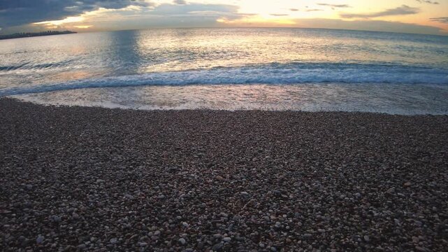 4K Close view of a wave breaking on a pebble shore along the Mediterranean coast in Antalya, Turkey. Foamy water and rhythmic wave sounds highlight the natural motion of the sea