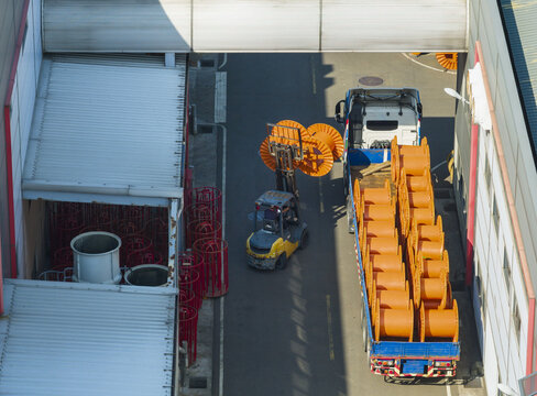 Aerial view of a forklift loading large orange cable reels onto a truck at a cable factory with industrial buildings and metal roofs in Taiwan.