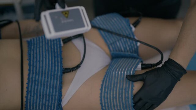 A woman receives an electro stimulation body treatment at a modern beauty salon. This professional procedure is designed for muscle toning and body contouring.