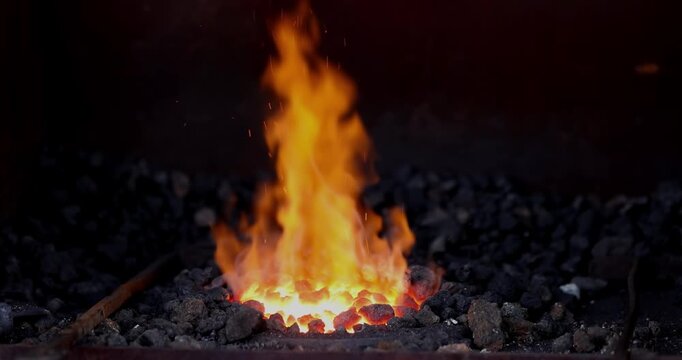 Vibrant orange flames ignite glowing charcoal in a blacksmith's forge, capturing the intense heat of traditional metalworking artistry.