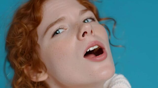 Close-up of a surprised young woman with red hair and blue eyes expressing shock and excitement.