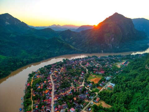 Aerial view of the village of Nong Khiaw nestled along the Nam Ou River surrounded by dramatic limestone karst mountains during a vibrant sunset in Nong Khiaw, Luang Prabang Province, Laos.