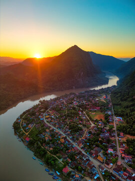 Aerial view of the town of Nong Khiaw nestled along the Nam Ou river with limestone mountains and a vibrant sunset in Nong Khiaw, Luang Prabang Province, Laos.