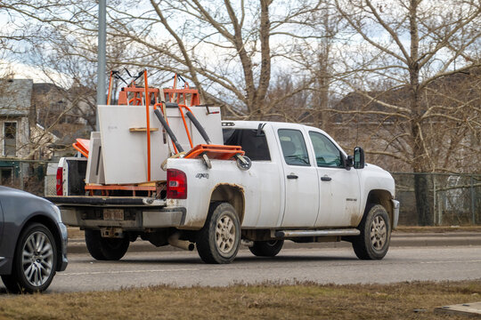 Calgary, AB, Canada. April 15, 2026. White Chevrolet pickup truck transporting construction materials and orange dollies on a suburban road.