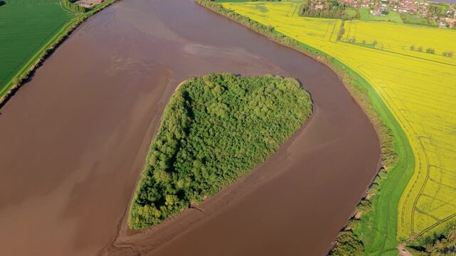 Aerial drone view of Howden Dyke Island surrounded by the brown muddy estuary water of the River Ouse and a green rural landscape in sunny conditions near Goole East Yorkshire UK