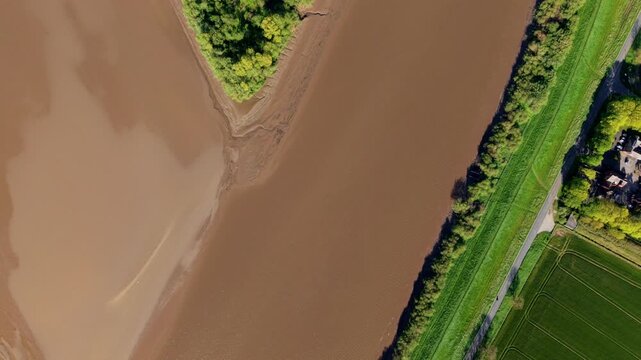 Aerial drone view of Howden Dyke Island surrounded by the brown muddy estuary water of the River Ouse and a green rural landscape in sunny conditions near Goole East Yorkshire UK