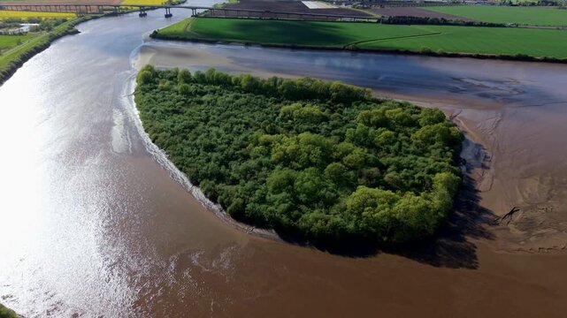 High angle drone view of the green Howden Dyke Island sitting in the middle of the brown tidal estuary of the River Ouse near Goole Yorkshire UK