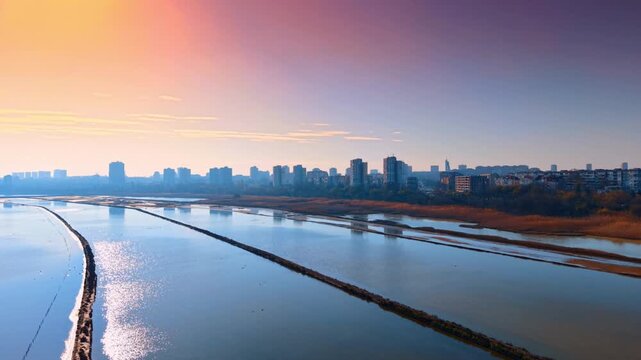 Aerial view of salt pans and wetlands at vibrant sunset. Drone shot of water reservoirs and salt evaporation ponds near the city during golden hour.