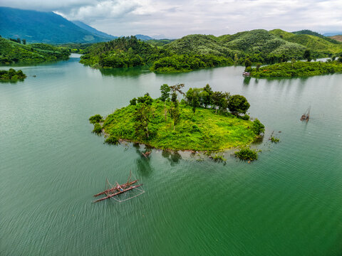 Aerial view of Nam Ngum Reservoir featuring a lush green island and traditional fishing lift nets on the calm water surface in Laos.