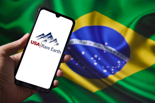 USA Rare Earth logo on a smartphone screen with the Brazilian flag in the background. The American mining company USA Rare Earth announced the purchase of the Brazilian mining company Serra Verde.