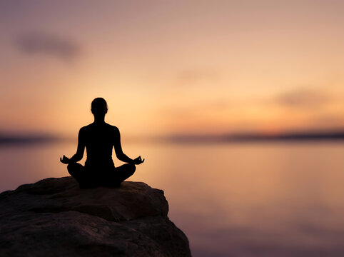 Serene Meditation at Sunset: A silhouette of a person sits in lotus position on a rock, with a background of a colorful sky and tranquil water. Capturing the peace and mindfulness of meditation.