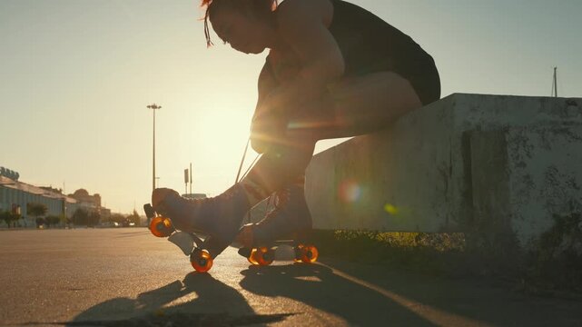 Tattooed woman tying roller skates at sunset