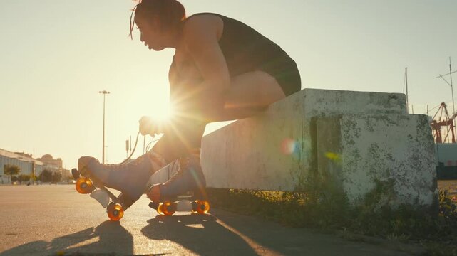 Woman preparing and lacing up roller skates at sunset