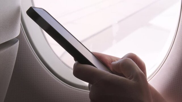 Woman passenger hands using smartphone while sitting by window on airplane during flight, Wi-Fi access service on board an aircraft