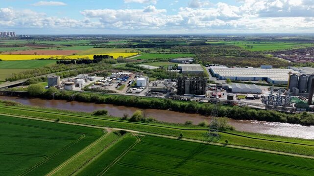 Drone shot of a large production plant complex featuring vertical storage silos and pipelines next to a river